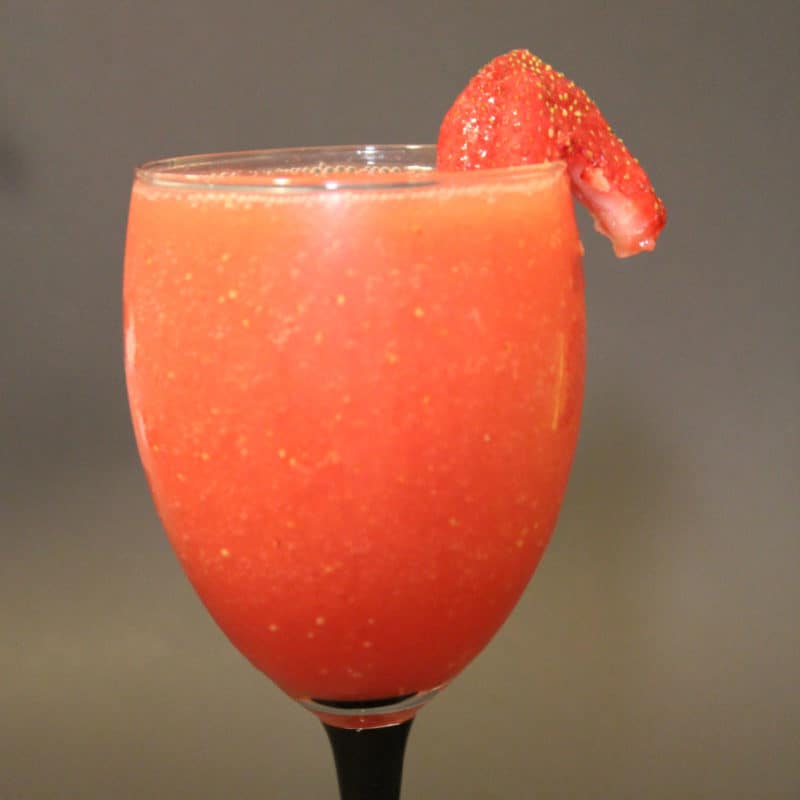 Coral Reef cocktail with a strawberry garnish in a champagne glass