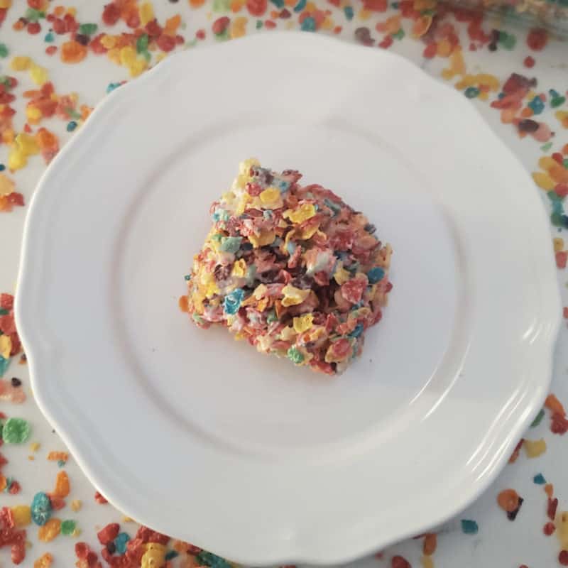Fruity Pebbles Treat square on a white plate surrounded by Fruity Pebbles