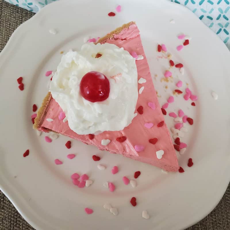 Slice of pink Kool Aid Pie on a white plate with heart sprinkles