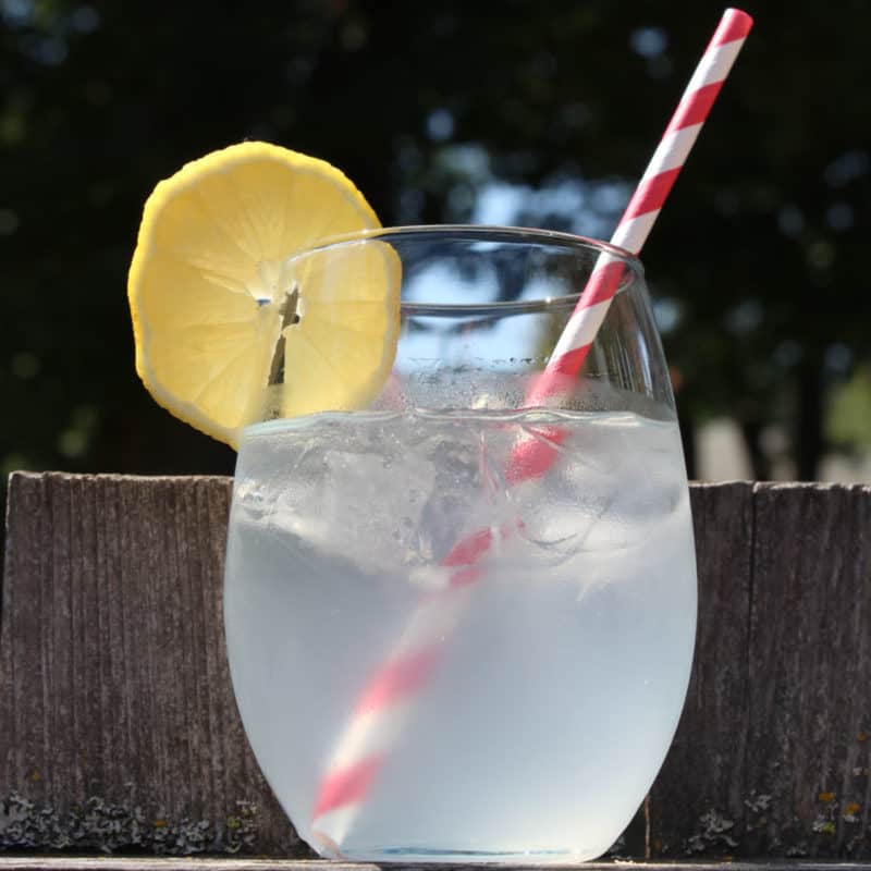 Mango Passionfruit Lemonade cocktail in a clear glass with lemon wheel and red striped straw