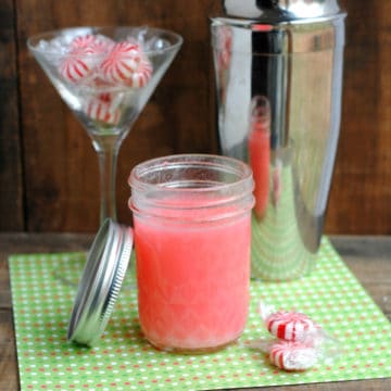 Peppermint vodka in a mason jar next to a martini glass with peppermint candies and a silver cocktail shaker