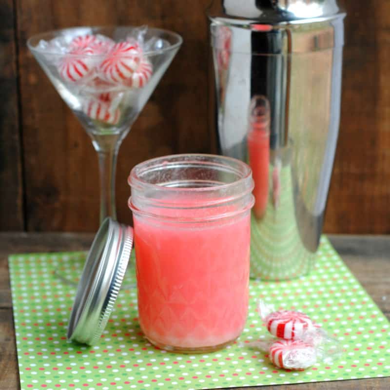 Peppermint vodka in a mason jar next to a martini glass with peppermint candies and a silver cocktail shaker