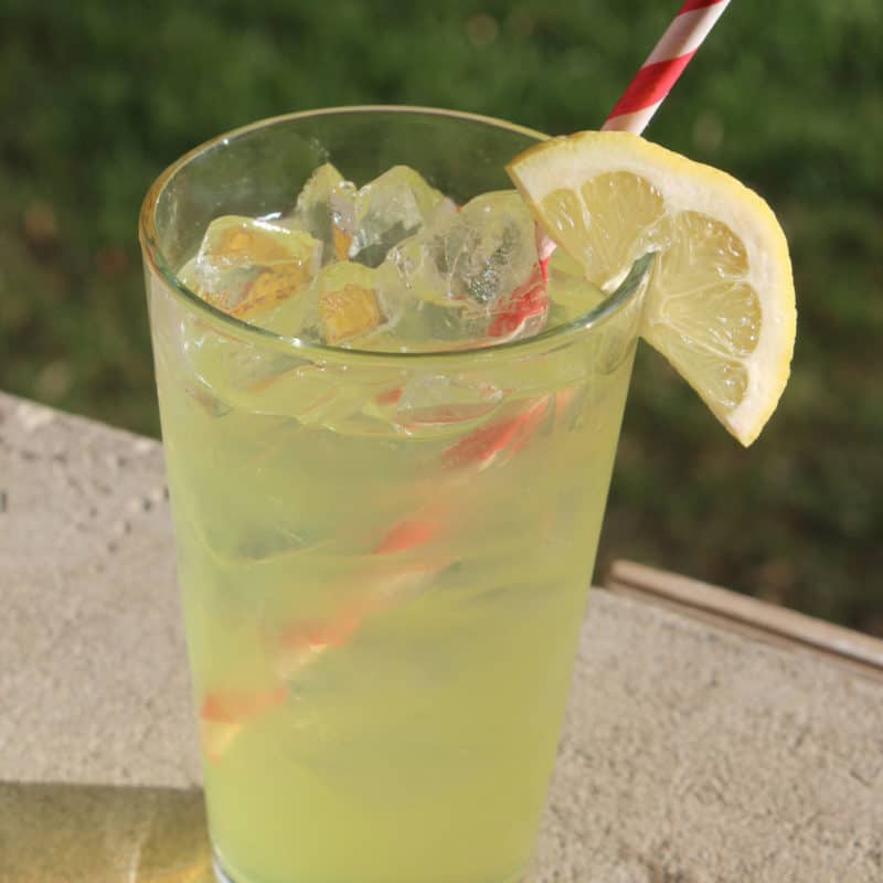 Twisted Lemonade cocktail in a tall glass with lemon wedge garnish and red striped straw