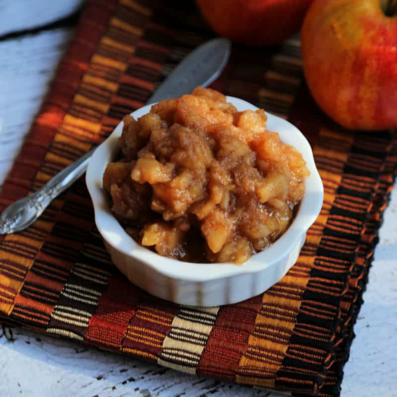 Chunky apple butter in a white ramekin next to a knife and apples