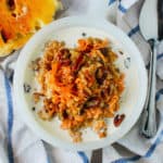 Carrot cake oatmeal in a white bowl next to a spoon and bagel