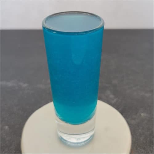 Blue cocktail shot on a white coaster.
