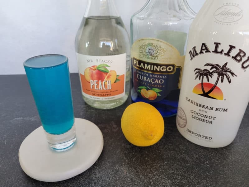 Blue shot next to peach schnapps, blue curacau, malibu coconut rum, and a lemon