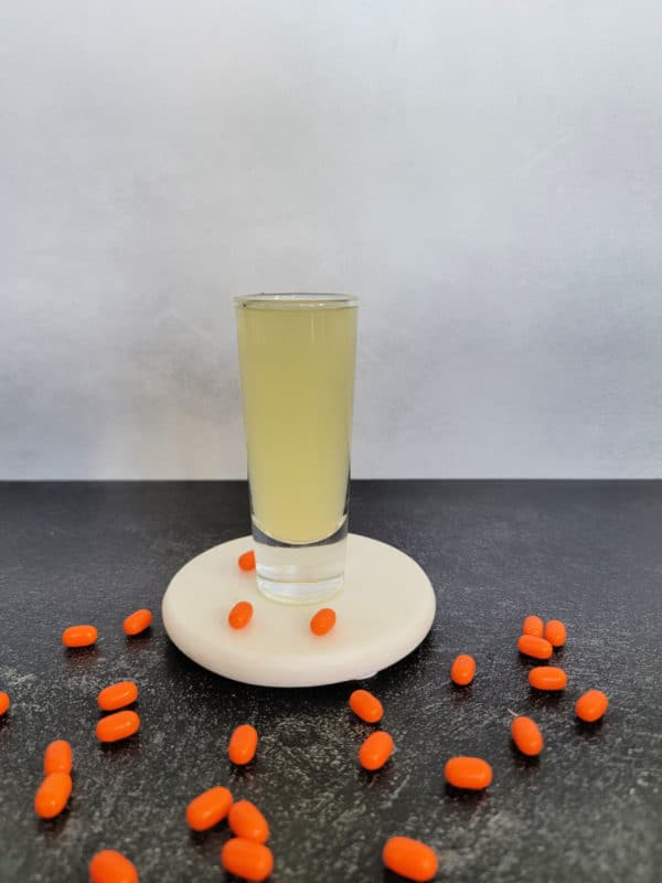 yellow shot on a white coaster surrounded by orange tic tacs