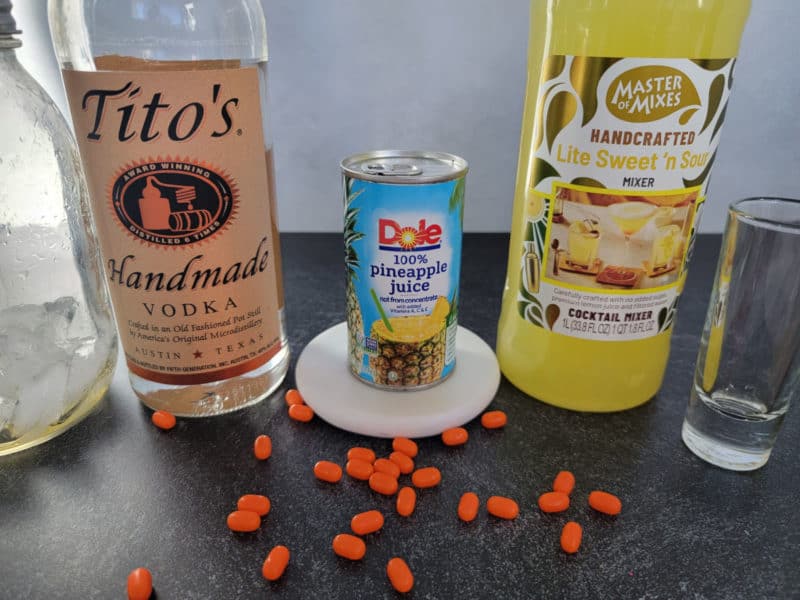 Tito's Vodka, Pineapple Juice, Sweet n Sour Mix next to a shot glass and orange tic tacs