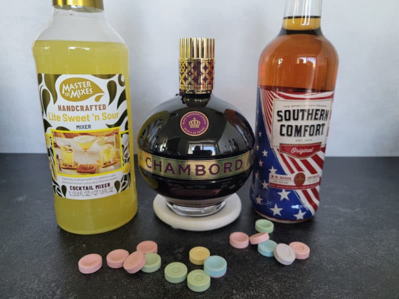 A bottle of Lite sweet and sour mix, Chambord, and Southern Comfort with Sweet Tart Candies