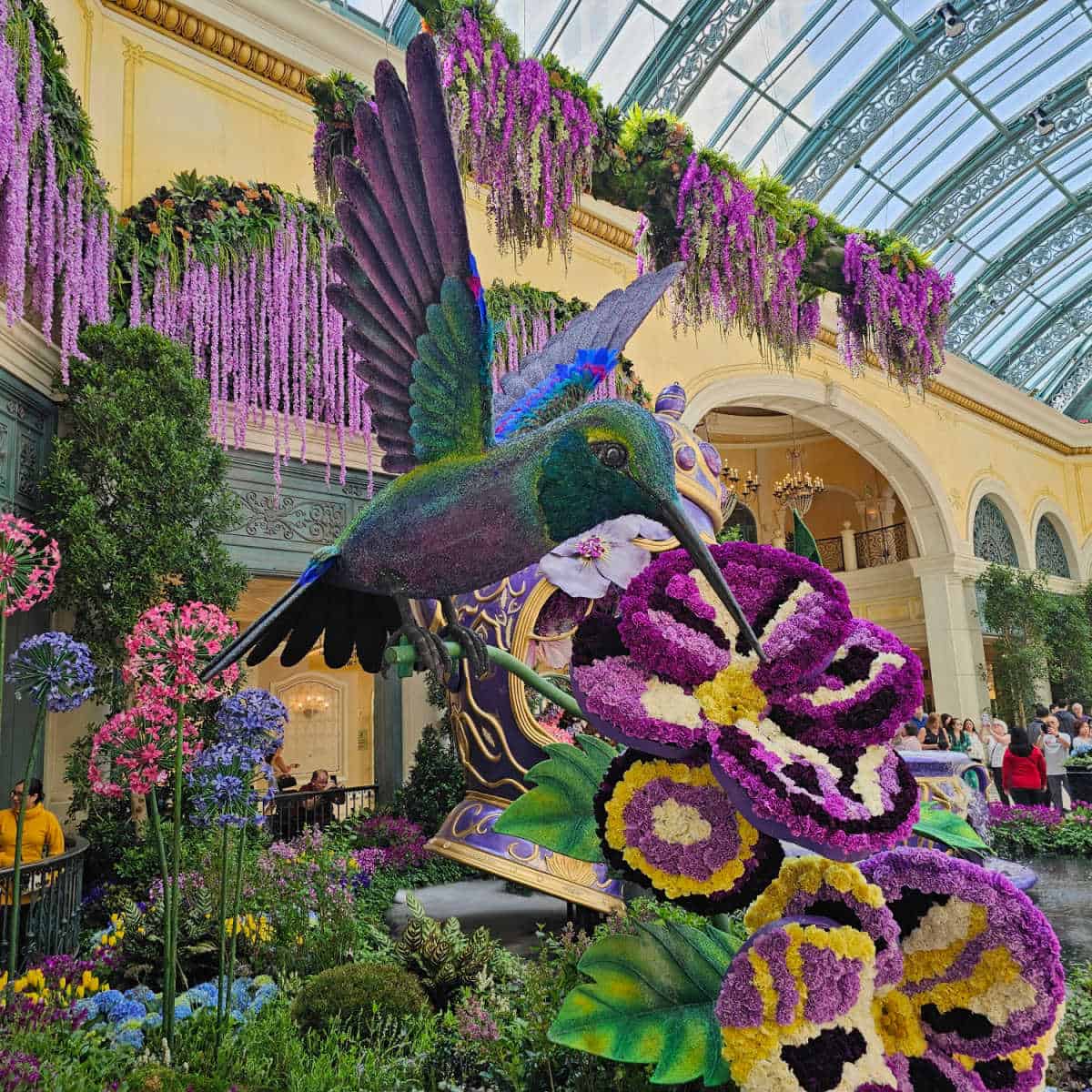 Purple hummingbird and flowers made out of flowers on display in the Bellagio Flower Garden with flowers hanging from the walls