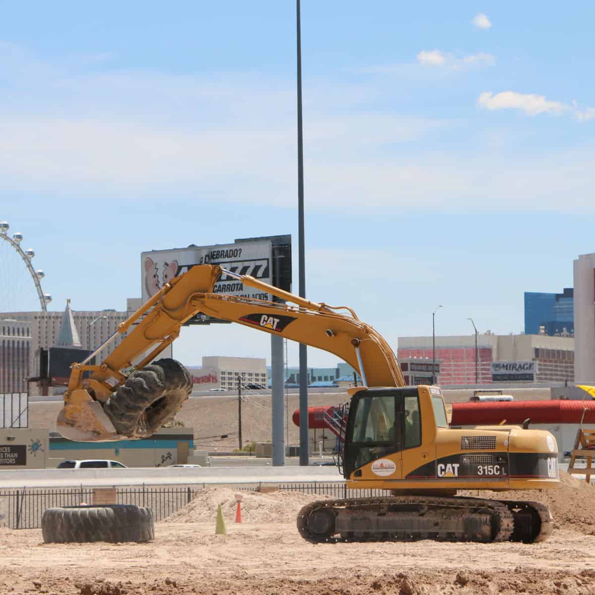 Excavator holding up a tire with the High Roller in the background