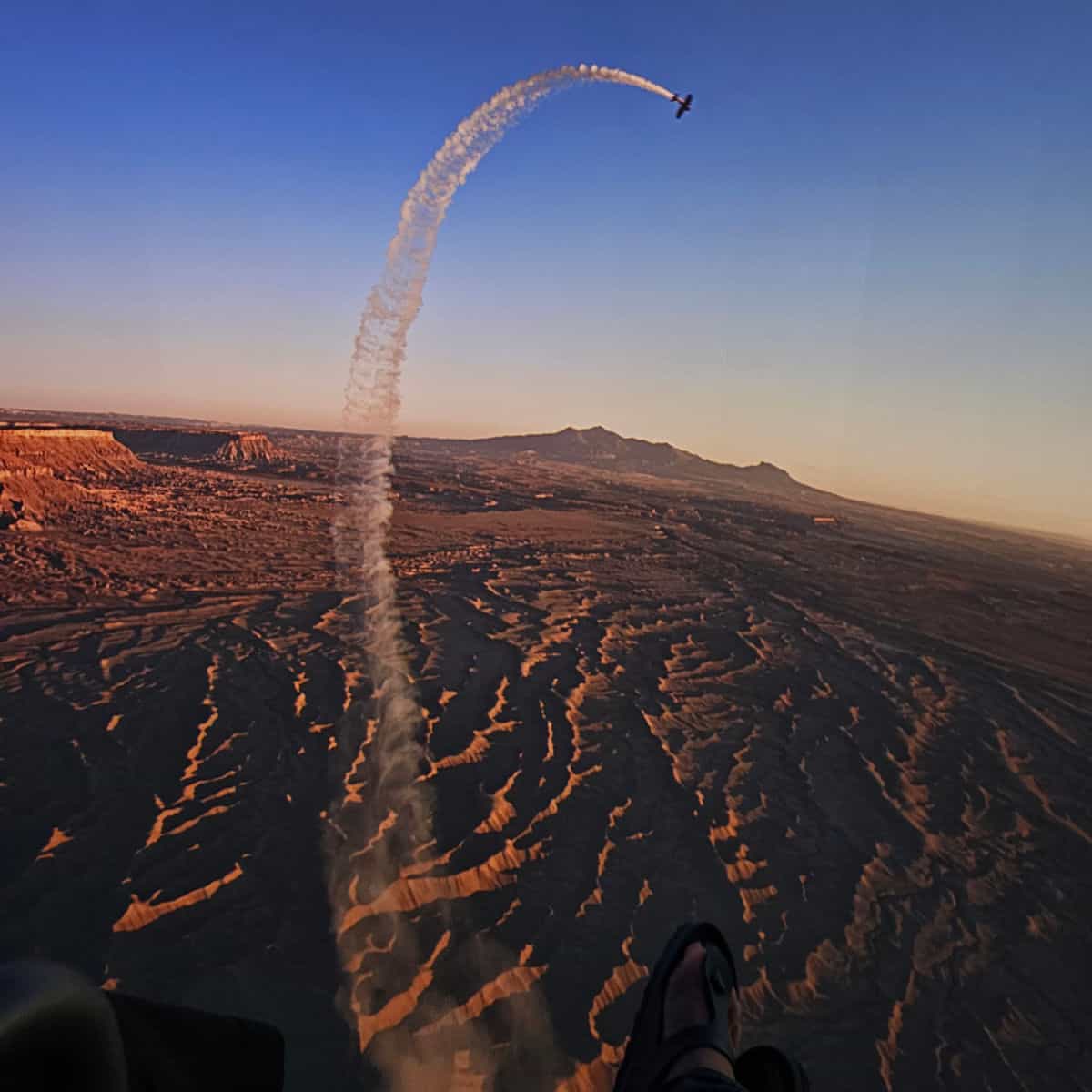 Plane with smoke trail flying over the American West. Feet in Birkenstock sandal at the bottom of the screen