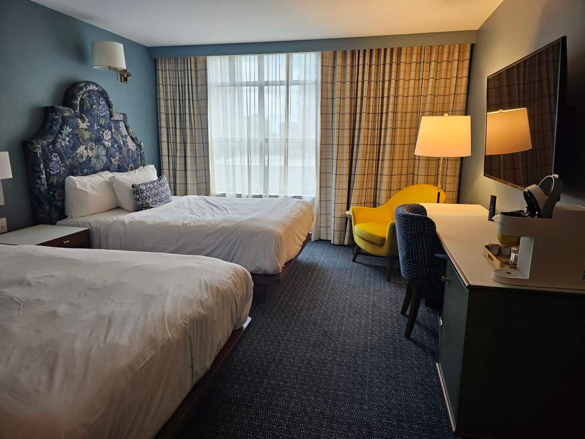two wueen beds, yellow chair next to a lamp, and work desk in Bradley hotel room