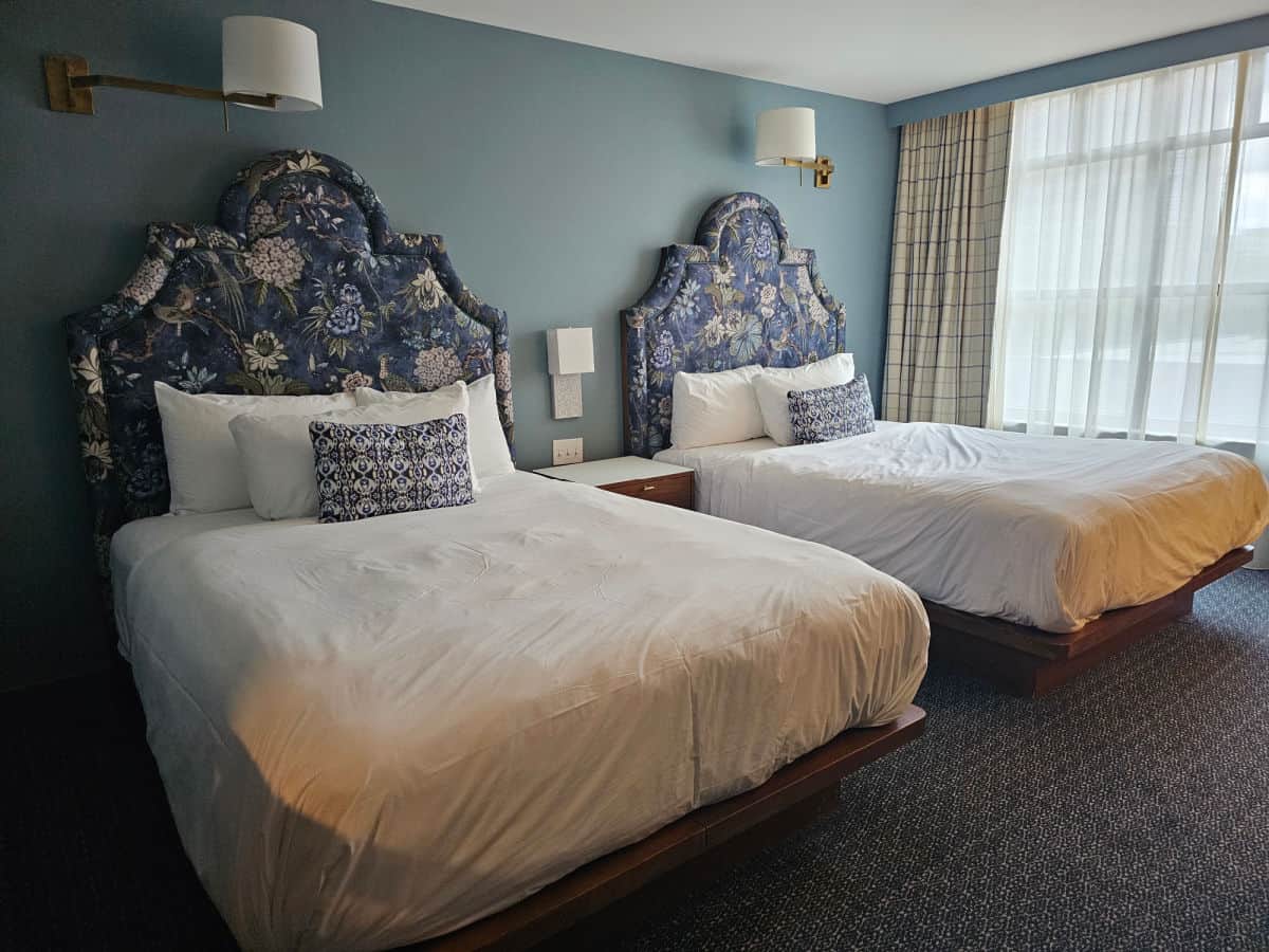 two queen beds with white linens, blue padded headboard