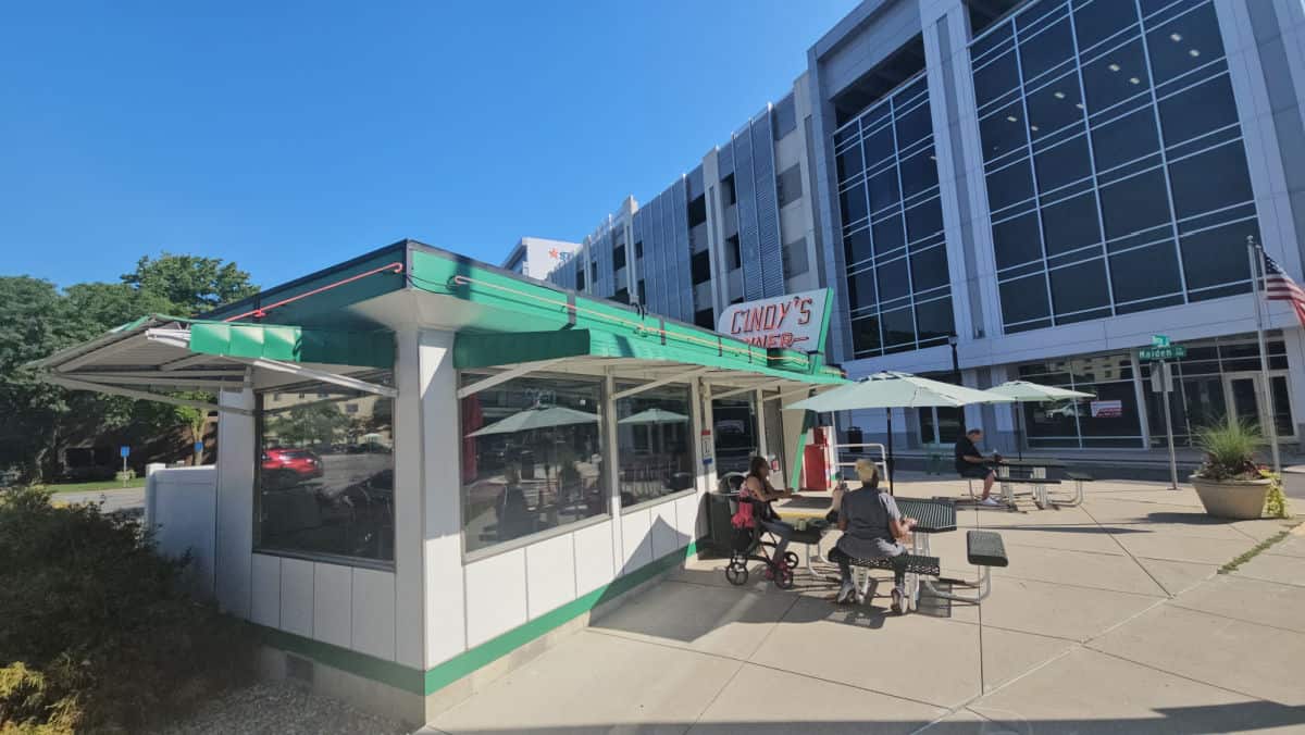 Cindy's Diner sign over the exterior of a white and green building with tables with green umbrellas outside