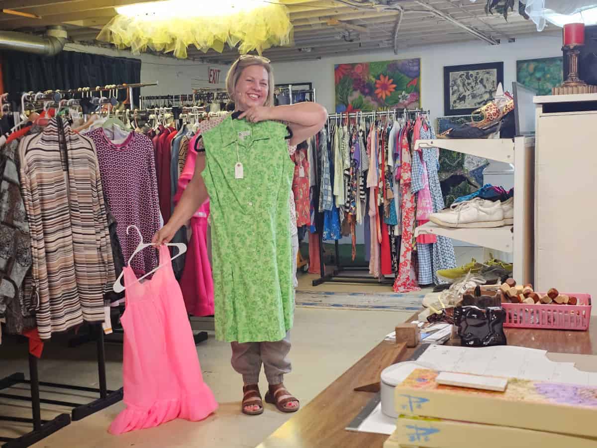 Kin holding a green dress and a pink dress in easy tiger vintage store