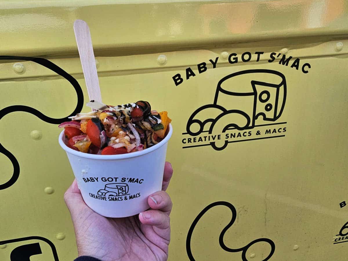 hand holding a cup of Italia Mac in front of the Baby Got S'Mac yellow logo