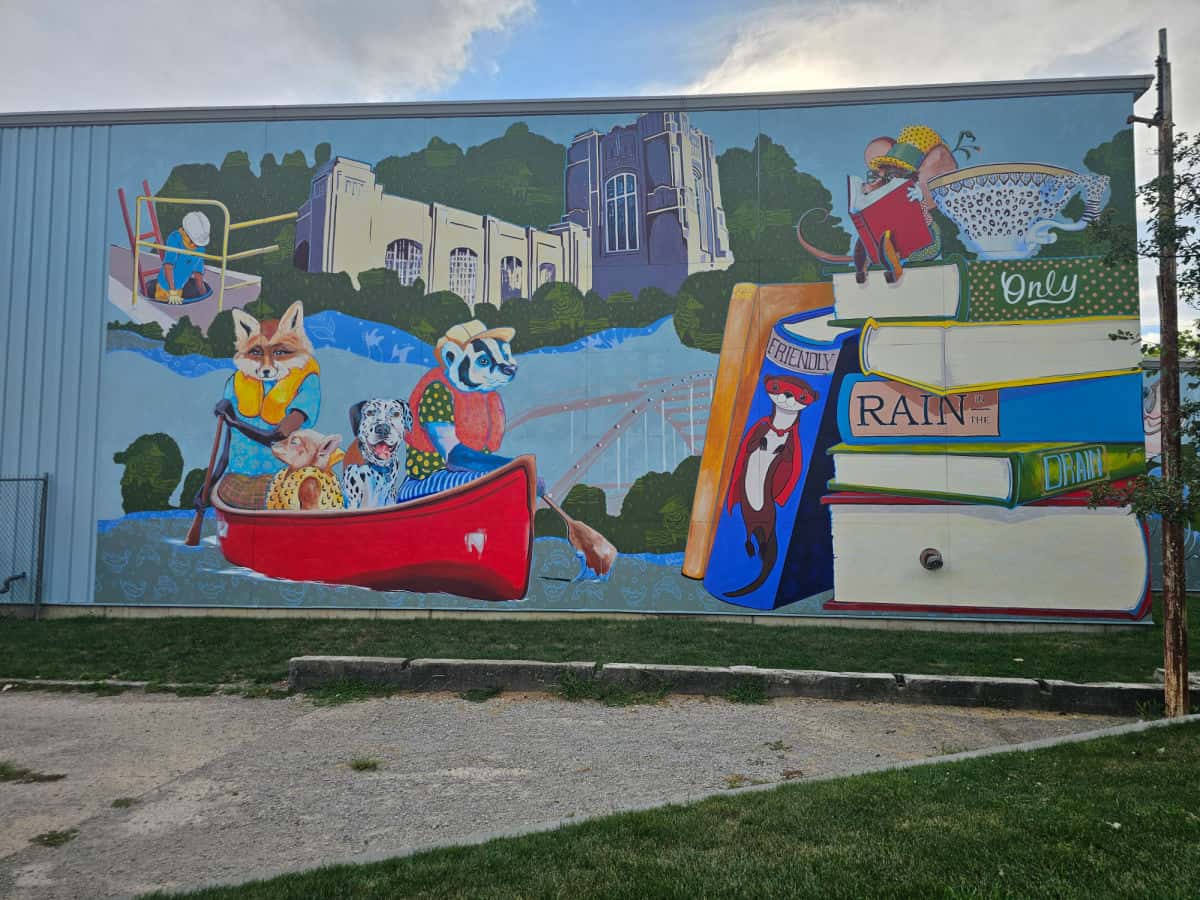Large building mural with a red canoe and wildlife in the canoe, stack of books with wildlife and fort wayne buildings