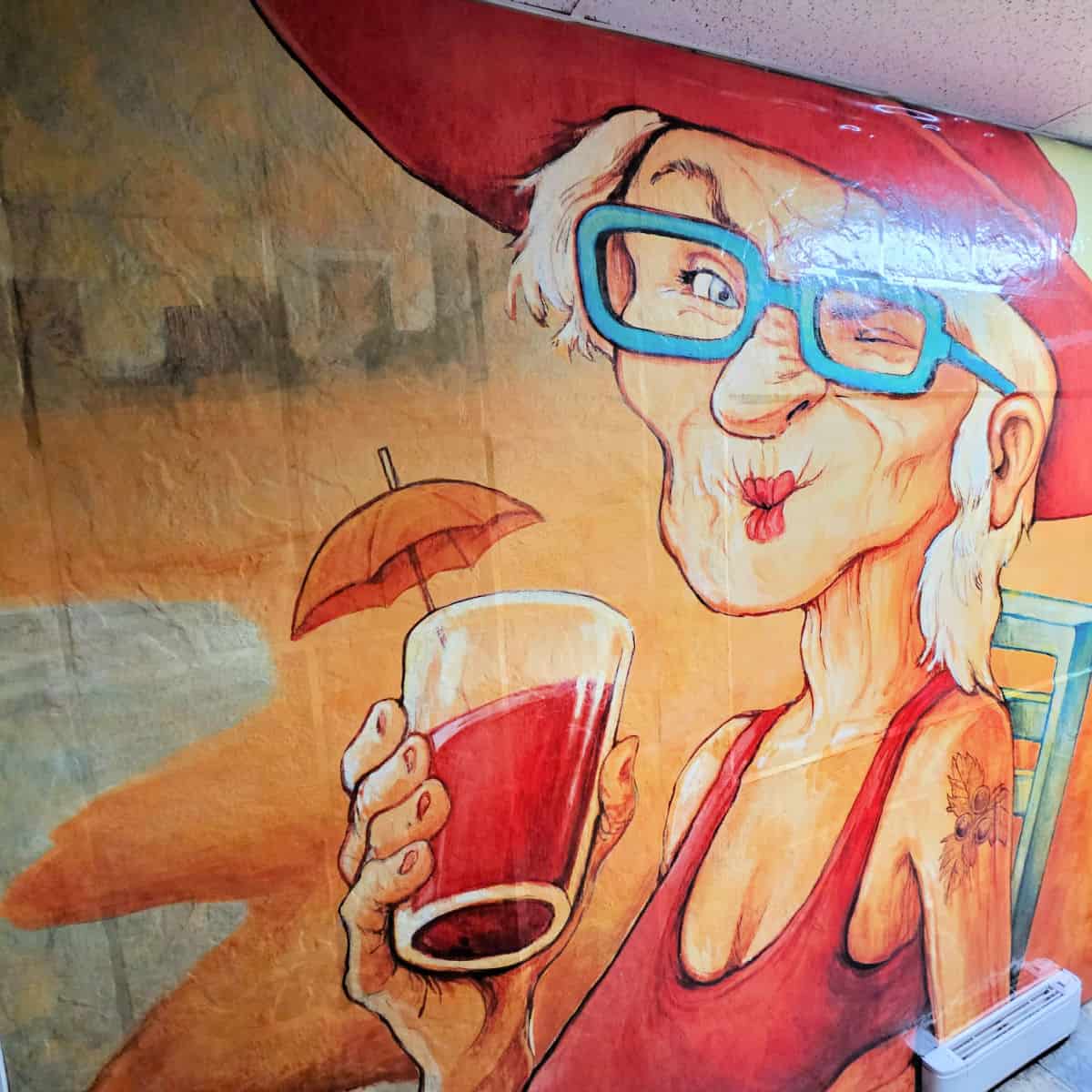 wall art with older woman holding a drink with an umbrella in it on the beach