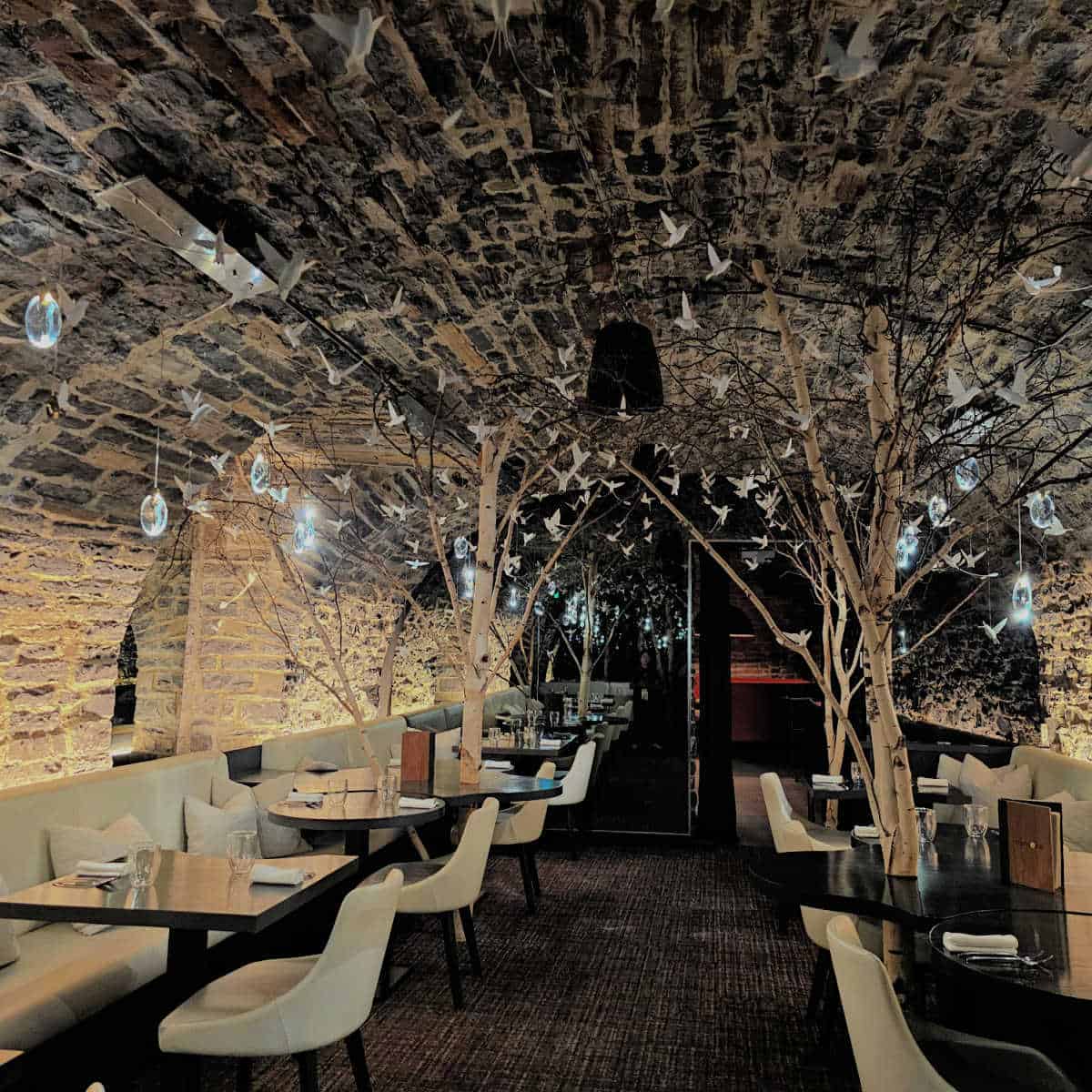 cave room with paper birds and globes hanging from the ceiling, white tables and benches, in Restaurant Tanière3