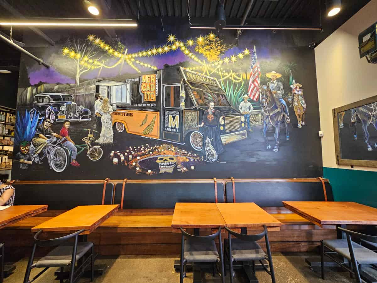 mural with figures next to the Mercado Food Truck over tables and a long bench