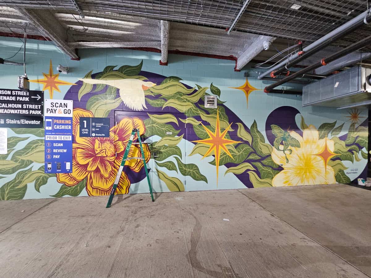 mural in progress with a bird and flowers, ladder in front of the mural
