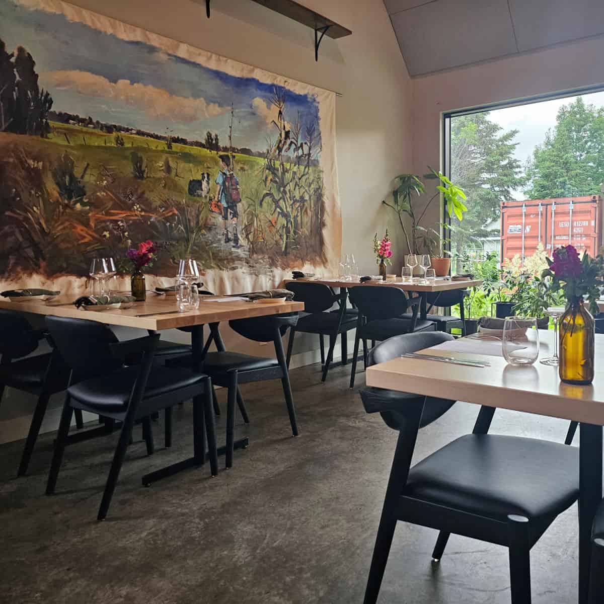 Au Paturage dining area with a painting on the wall of a boy with a dog in a field, tables have flowers and place settings on them.