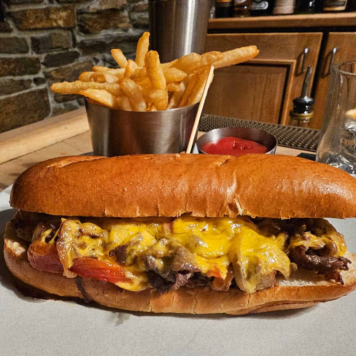 gourmet cheesesteak with a silver cup full of fries and a ramekin of ketchup at the Cellar Bar