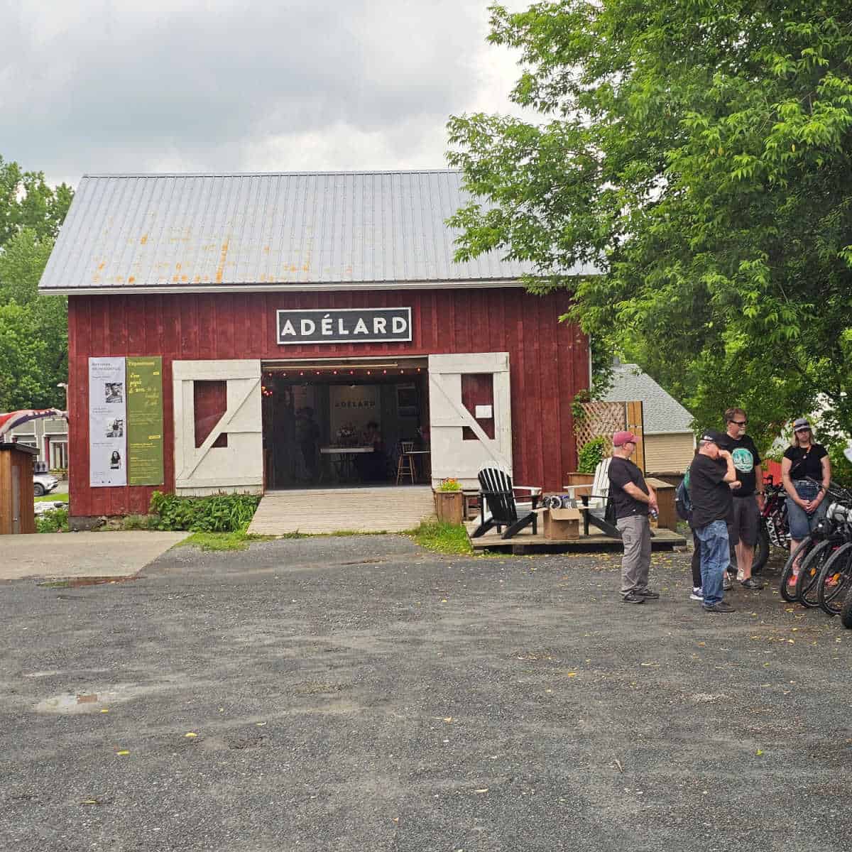 Adelard sign over a red bar with wide open barn doors, group of people standing next to e-bikes