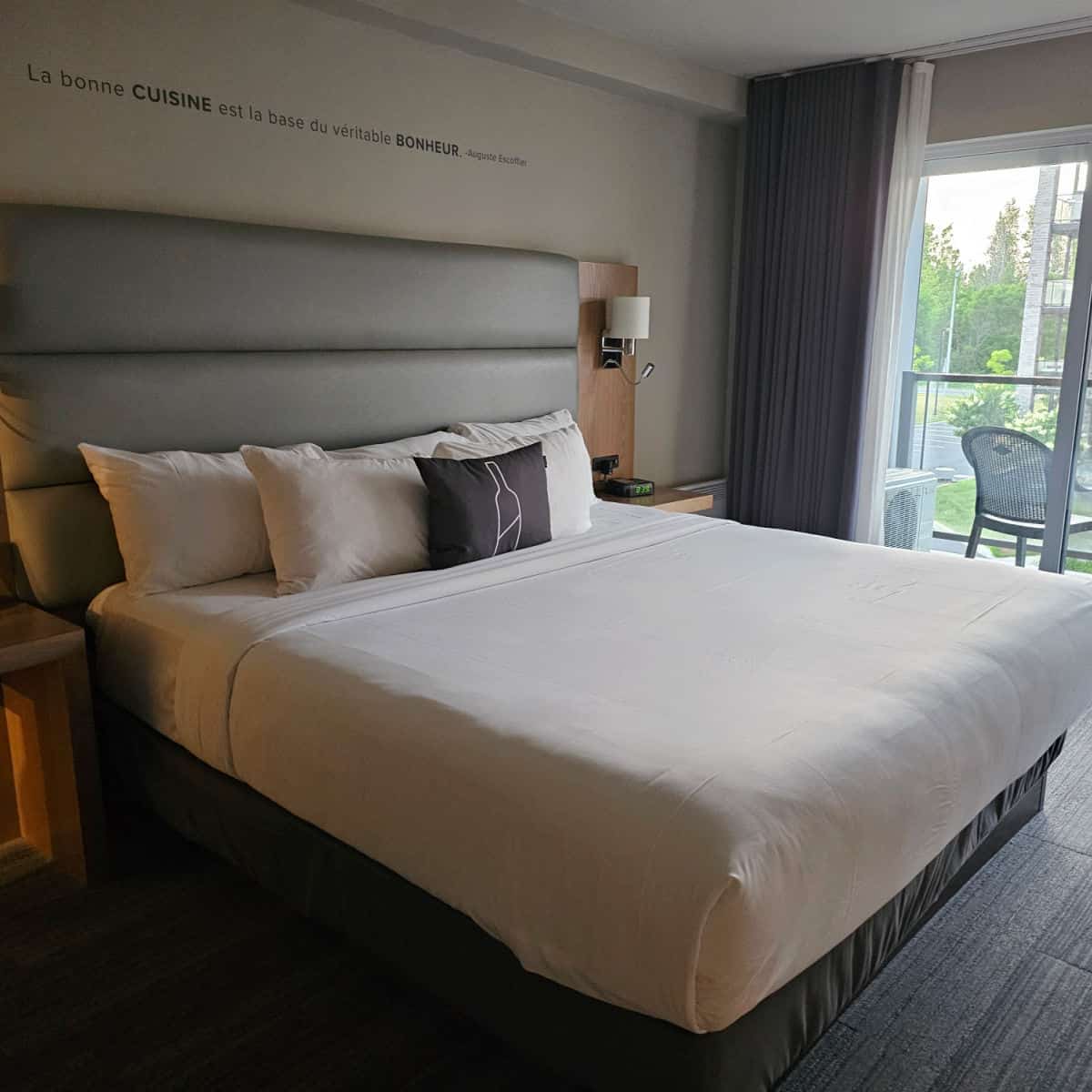 king bed with a pillow with a wine bottle on it, saying on the wall - La Bonne Cuisine est la Base du veritables Bonheur