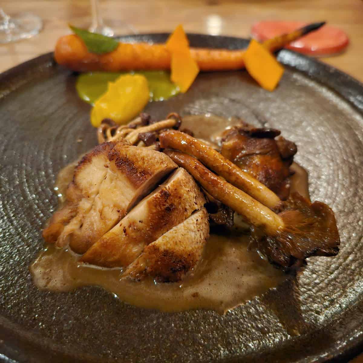 Mushroom dish with sauce next to carrots on a dark plate at Espace Old Mill