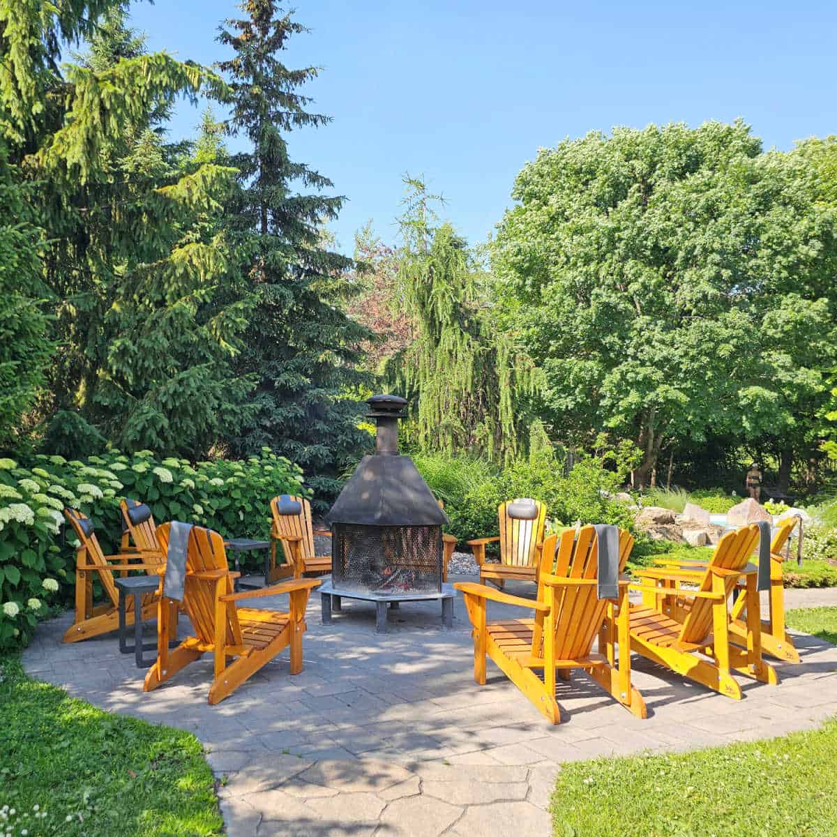 Outdoor fireplace with orange Adirondack chairs surrounding it with trees and bushes around Strøm Spa Nordique Mont-Saint-Hilaire