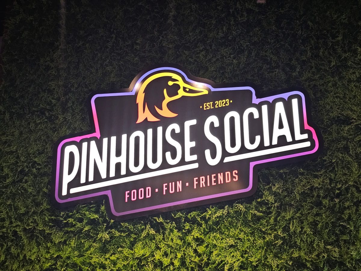 Pinhouse Social Food Fun Friends logo on a fake grass wall