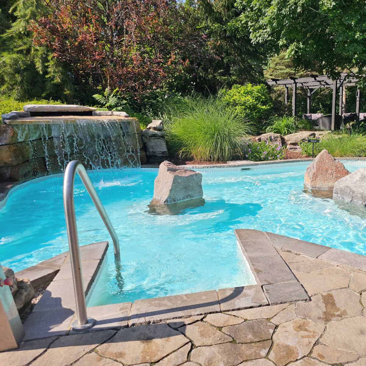outdoor pool with a waterfall, rocks in the pool, and lounging area behind it at Strøm Spa Nordique Mont-Saint-Hilaire