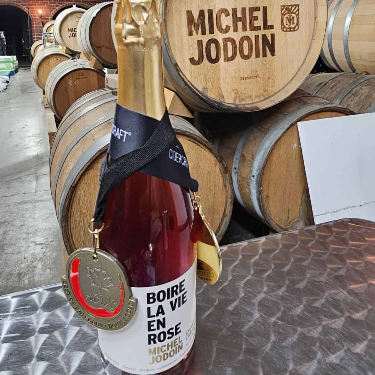 Cidrerie Michel Jodoin Rose with award sitting on a counter near wine barrels labeled Michel Jodoin