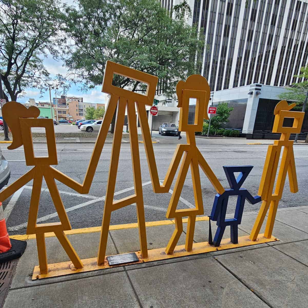 Yellow sculpture bike rack in the shape of a family holding hands with one child blue