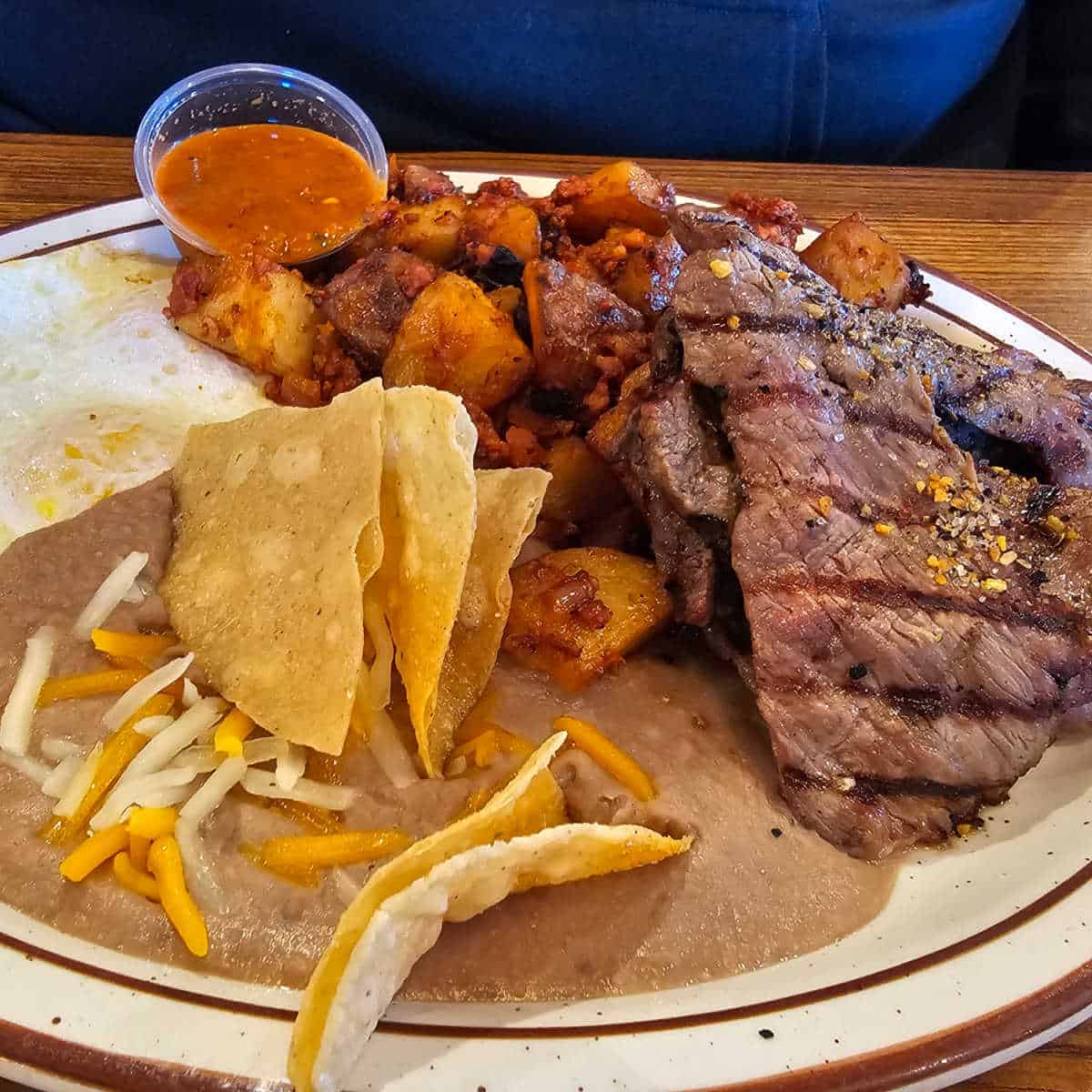 white plate with steak, breakfast potatoes, eggs, beans, chips, and a container of salsa from Mountain Oaks Cafe, Oakhurst