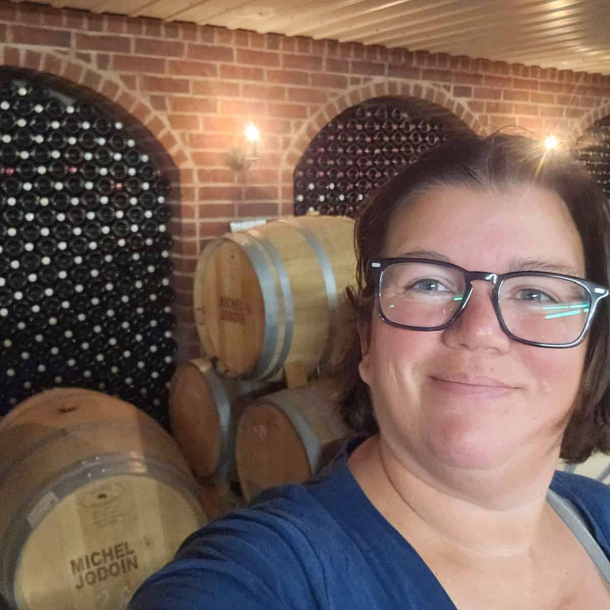 Tammilee at Cidrerie Michel Jodoin with wine barrels and a wall of wine bottles