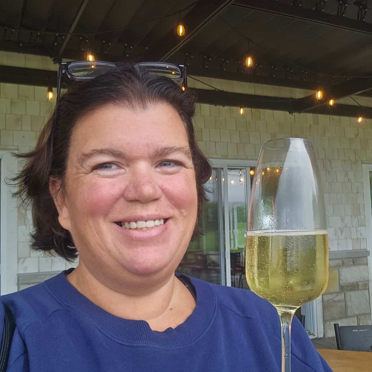 Tammilee smiling holding a glass of white sparkling wine at a vineyard