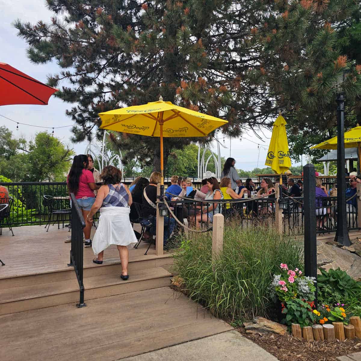 Outdoor seating with yellow umbrellas, people walking up stairs to reach a table, trees nearby