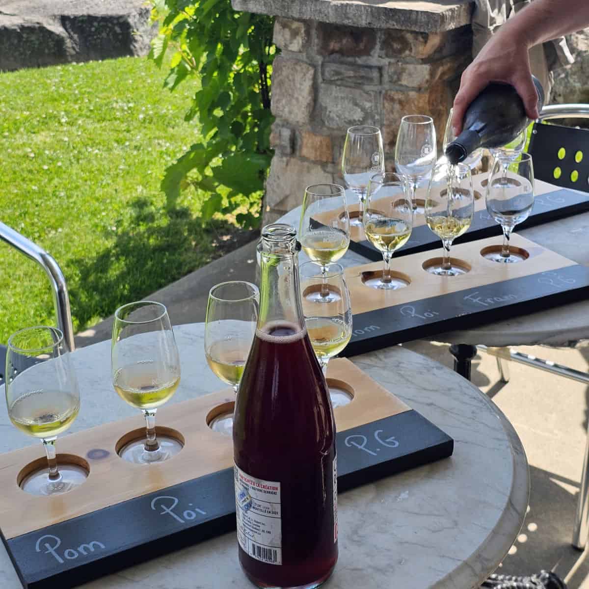 hand pouring white wine into glasses along boards with bottles of wine sitting next to the boards