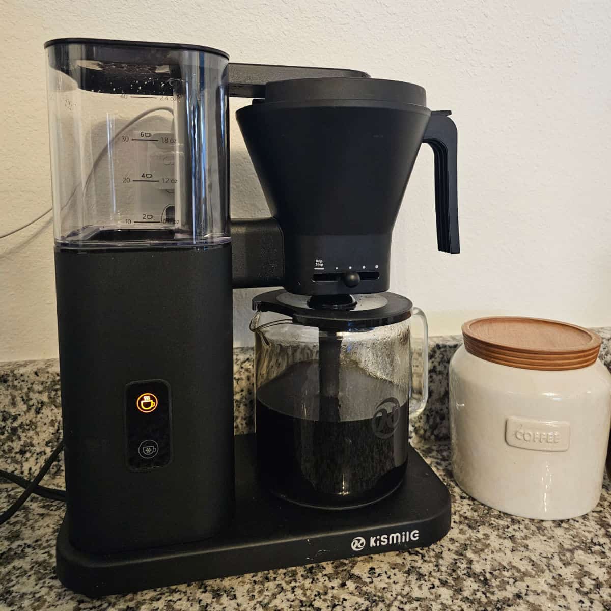 Kismile Coffee maker brewing next to a container with coffee on it