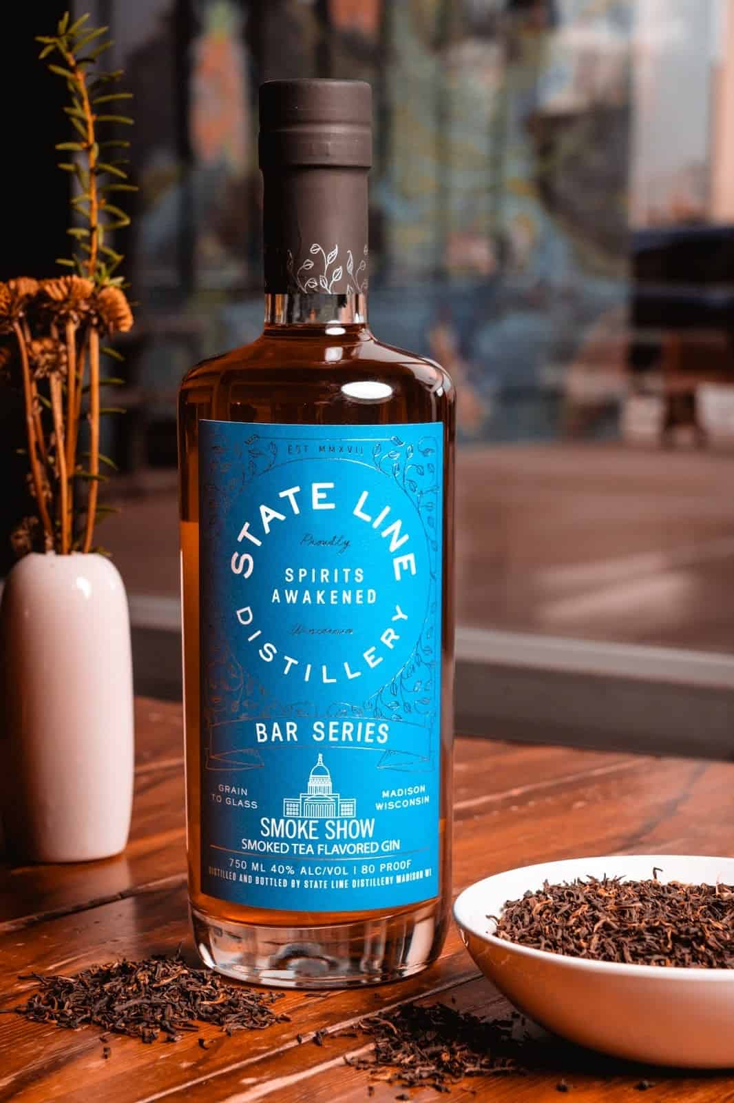 State Line Distillery Smoke Show Smoked Tea flavored Gin bottle next to a bowl of tea leaves