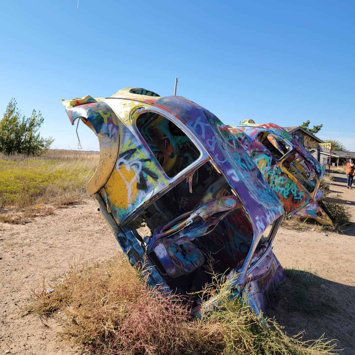 VW beetles covered in spray paint tilted on their hoods sticking out of the ground