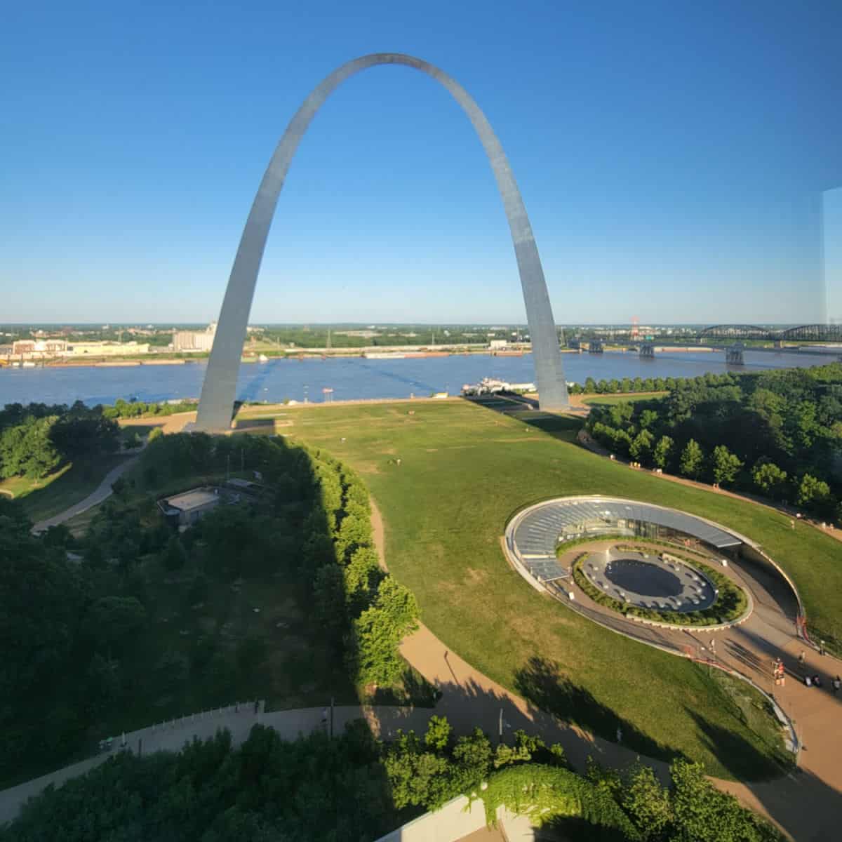 looking out to the Gateway Arch and grounds with the museum entrance on a blue sky day