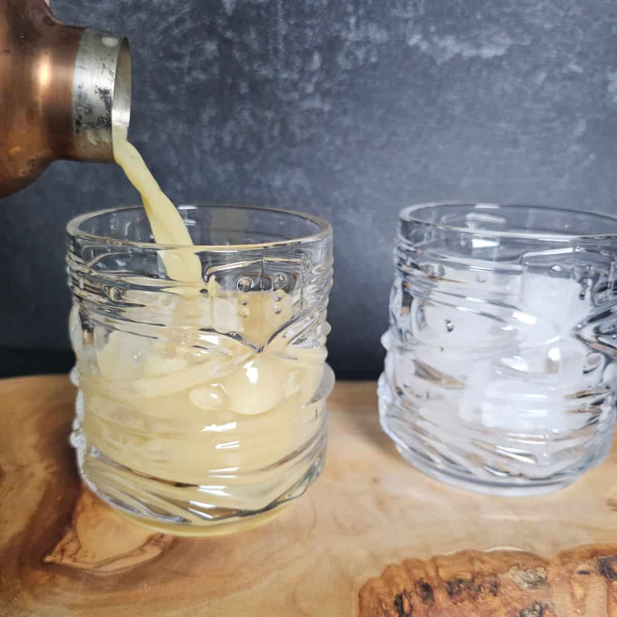 two tiki glasses with Painkiller Cocktails garnished with nutmeg sitting on a wooden board