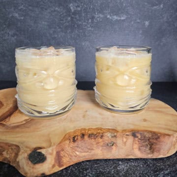 two tiki glasses with Painkiller Cocktails garnished with nutmeg sitting on a wooden board