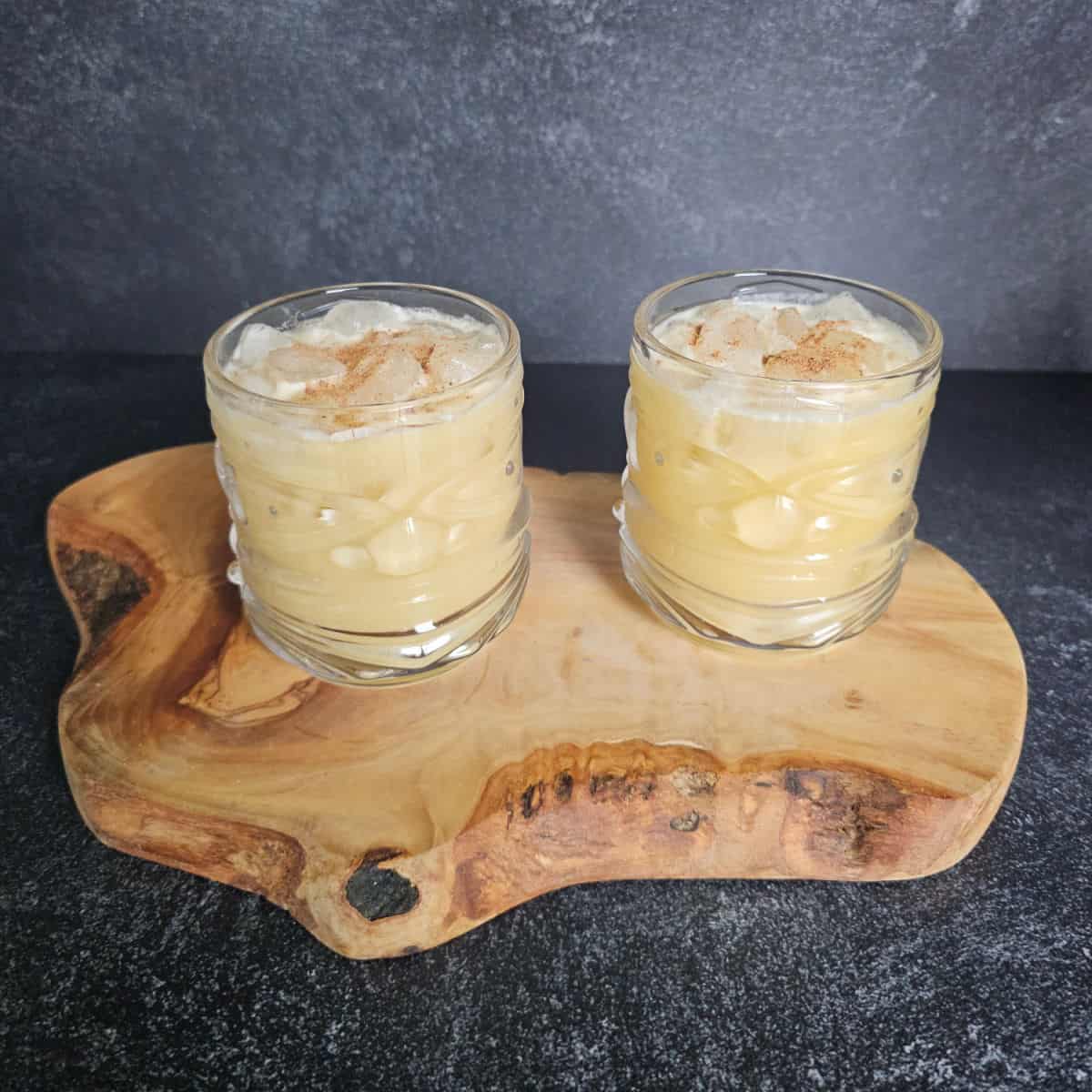 two tiki glasses with Painkiller Cocktails garnished with nutmeg sitting on a wooden board