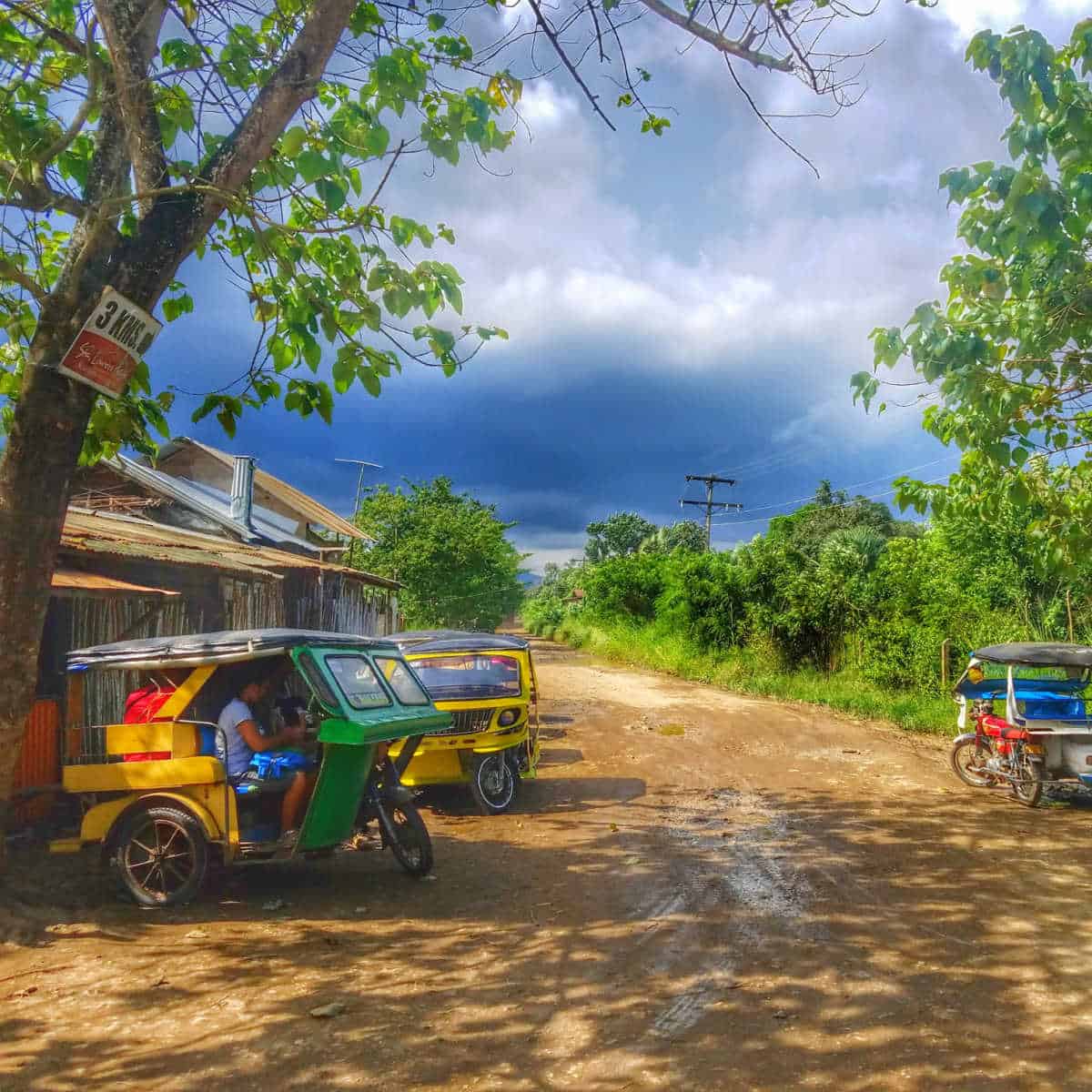 colorful trike taxis lined up on a dirt road with buildings next to them